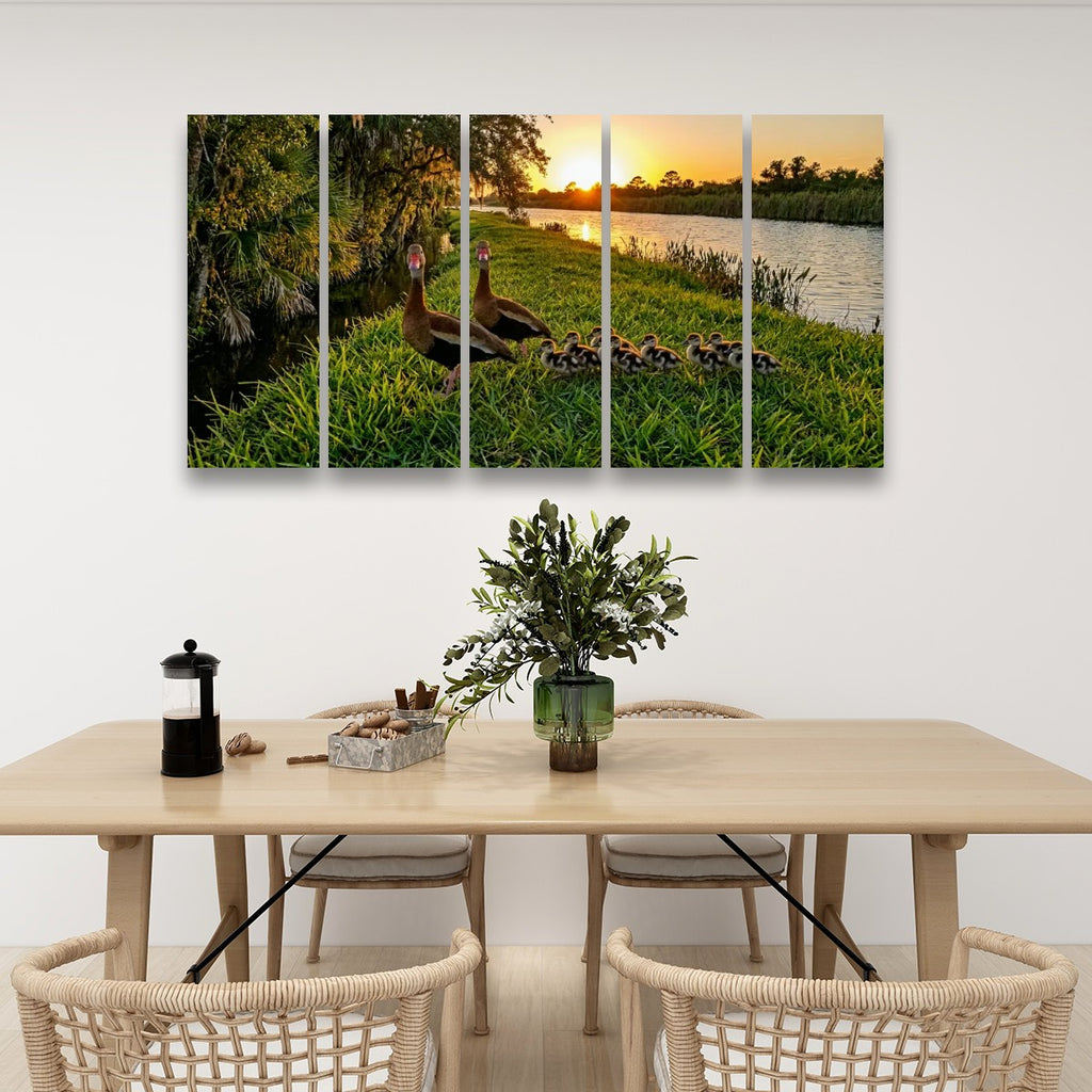 A five-panel canvas wall art set depicting a mother Black-bellied Whistling-Ducks by a lake at sunset, displayed on a white wall above a dining table with chairs.