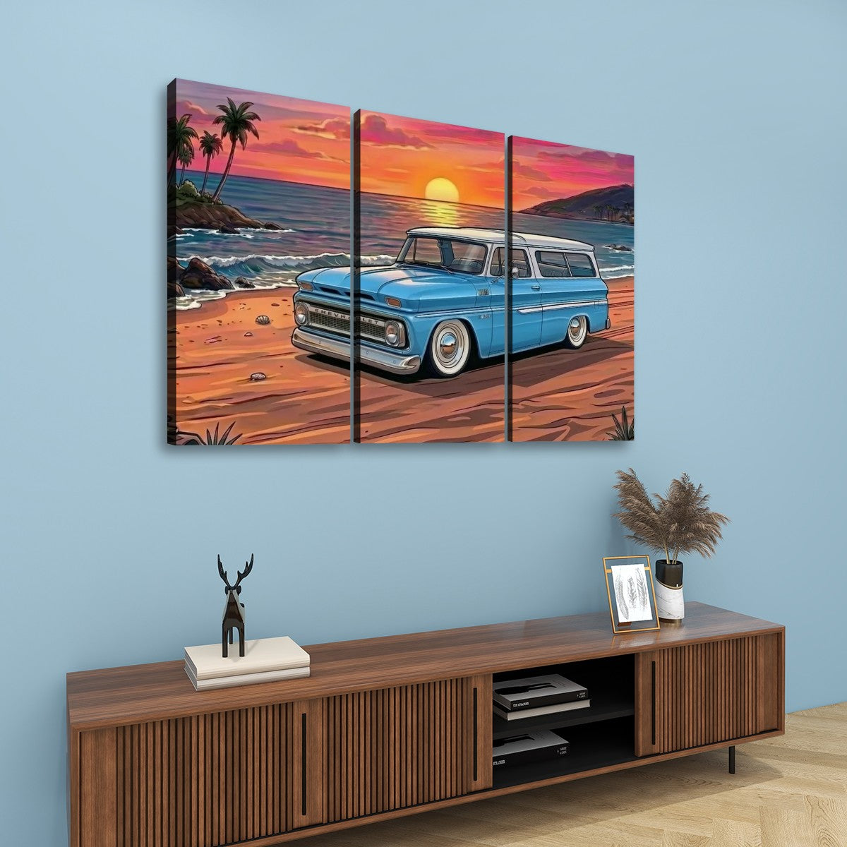 A three-panel canvas wall art print depicting a classic light blue 1966 Chevy Suburban station wagon parked on a beach at sunset, displayed on a light blue wall above a wooden console table.
