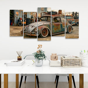 A 5-panel canvas wall art print depicting a vintage, rusted blue and green Volkswagen Beetle car in a workshop, displayed on a white wall above a styled dining table with books, a vase, and a basket.