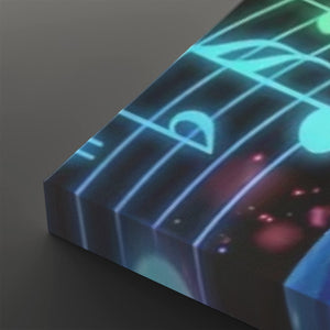 A close-up of a rectangular panel or block printed with a glowing musical staff and note design in cyan, blue, purple, and pink on a dark background, photographed against a dark gray studio backdrop.