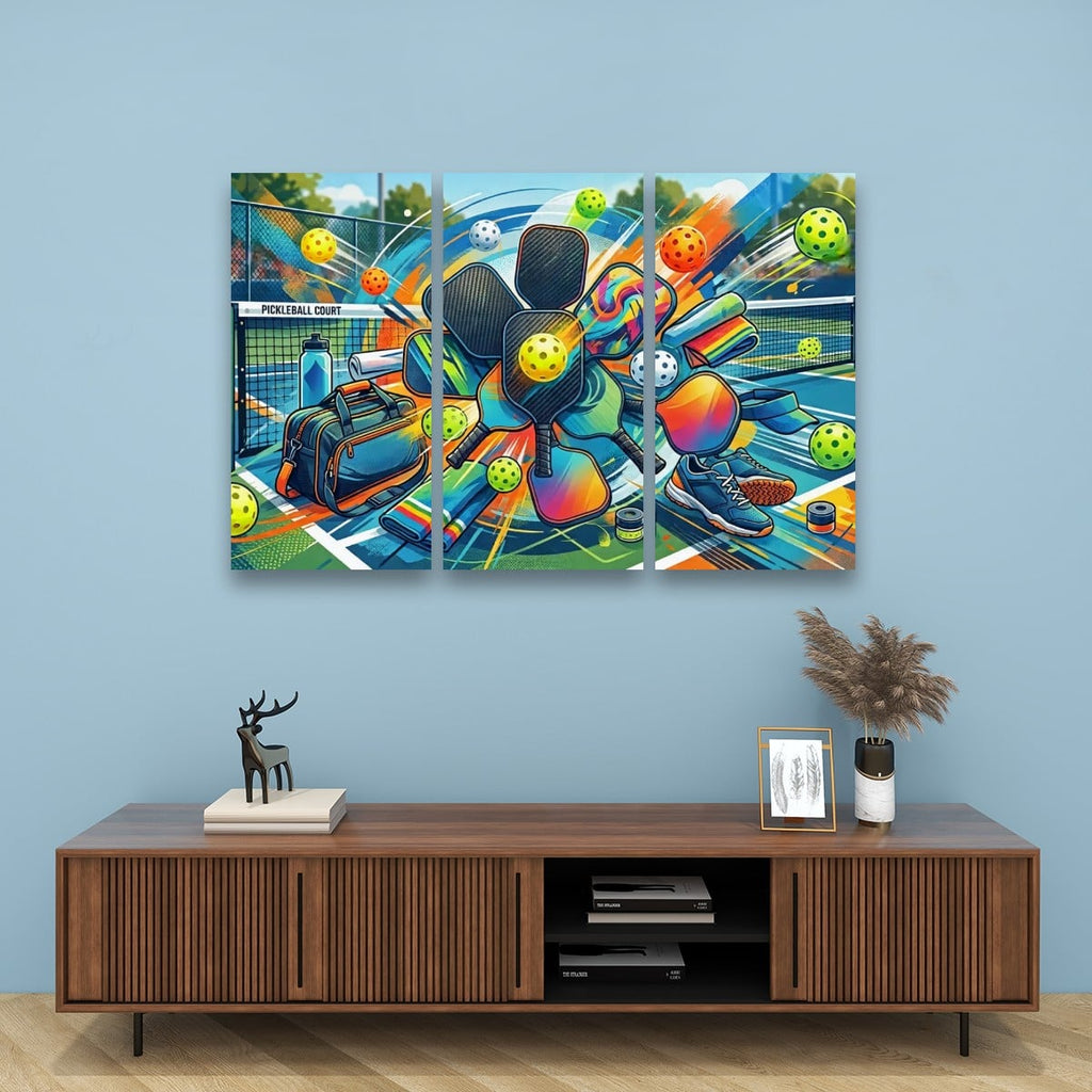 A three-panel canvas wall art print depicting a colorful pickleball-themed action scene, displayed on a light blue wall above a wooden console table with decorative items.