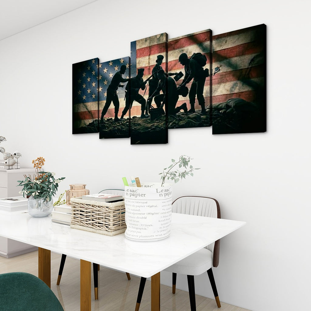A 5-panel canvas wall art set depicting silhouetted soldiers carrying a body against an American flag background, displayed on a white wall above a dining table in a modern room setting.