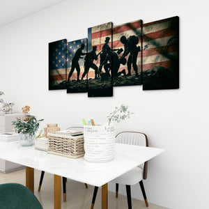 A 5-panel canvas wall art set depicting silhouetted soldiers carrying a body against an American flag background, displayed on a white wall above a dining table in a modern room setting.