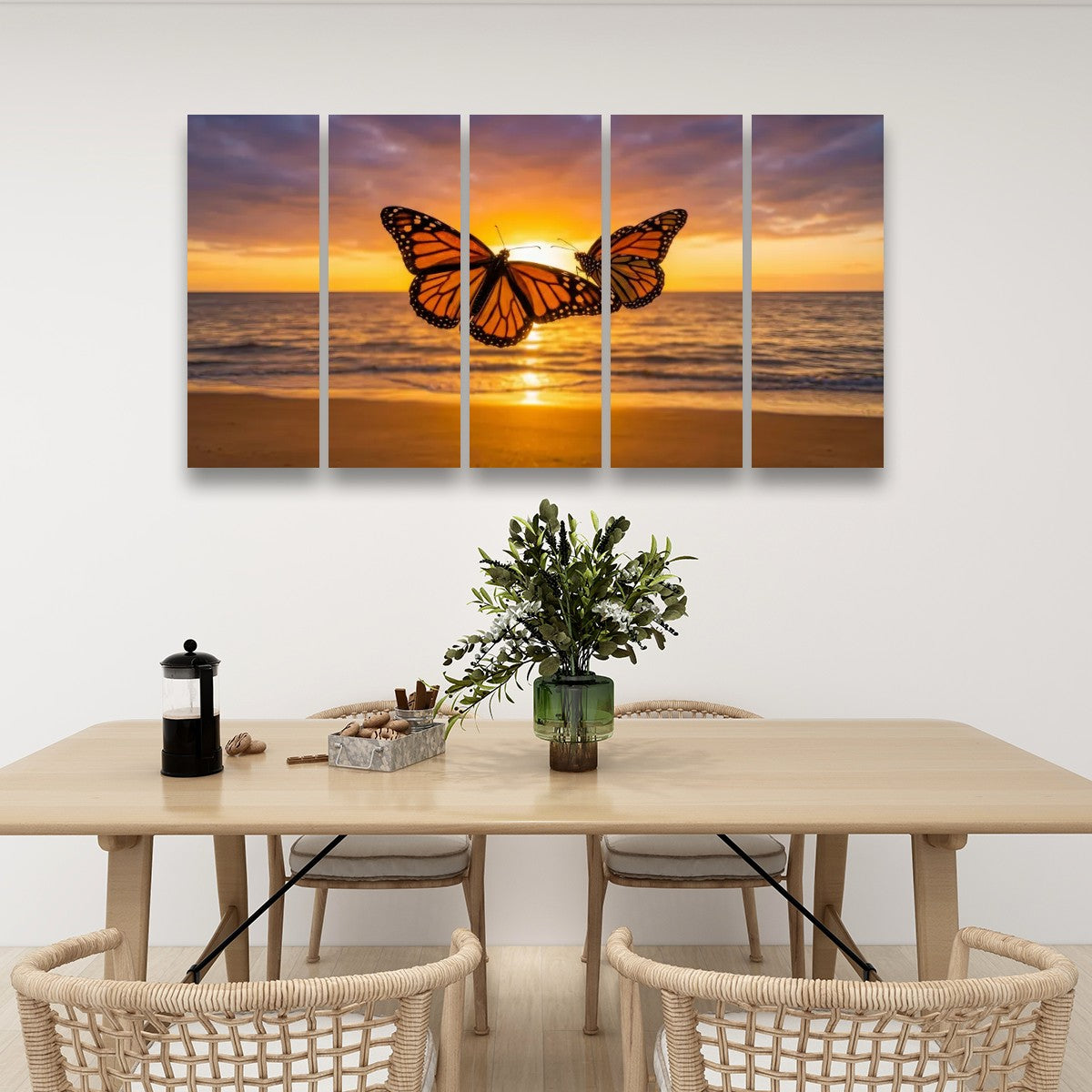 A five-panel canvas wall art set depicting a monarch butterfly over an ocean sunset, displayed on a white wall above a dining table with chairs.
