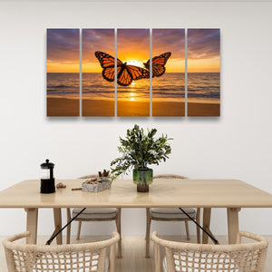 A five-panel canvas wall art set depicting a monarch butterfly over an ocean sunset, displayed on a white wall above a dining table with chairs.