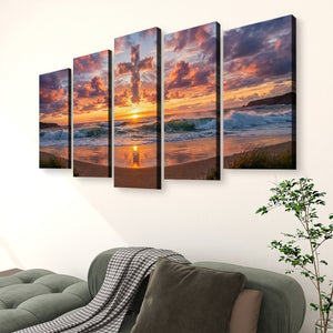 A five-panel canvas wall art set depicting a dramatic sunset over the ocean waves and sandy beach, displayed on a white wall above a green sofa with a throw blanket and a potted plant.