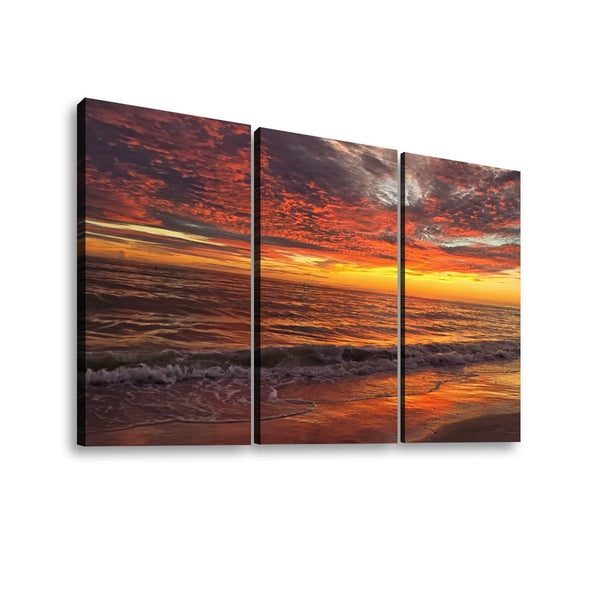 Three-panel canvas wall art showing a dramatic sunset over the ocean, with fiery orange and red clouds reflected in the water, displayed against a plain white background.
