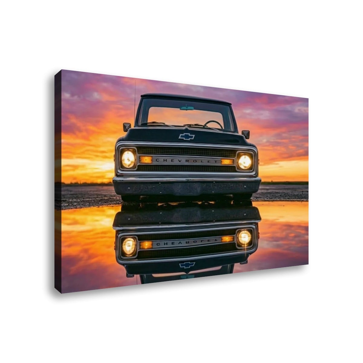 A square canvas wall art print showing a black 1970 Chevy C10 facing forward on a reflective surface at sunset, with a pink, orange, and purple sky. The canvas is photographed at a slight angle against a plain white background.