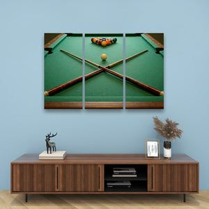 A three-panel canvas wall art print depicting a green pool table with crossed cues and a ball rack, displayed on a light blue wall above a wooden console table with decorative items.