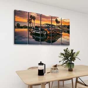 A five-panel canvas wall art set depicting a classic car on a beach at sunset, displayed on a white wall above a dining table with chairs, a French press, and a potted plant.