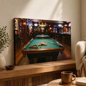 A large rectangular wall art print showing a pool table inside a dimly lit bar, displayed above a wooden console in a styled interior with a mug, plant, and armchair visible.