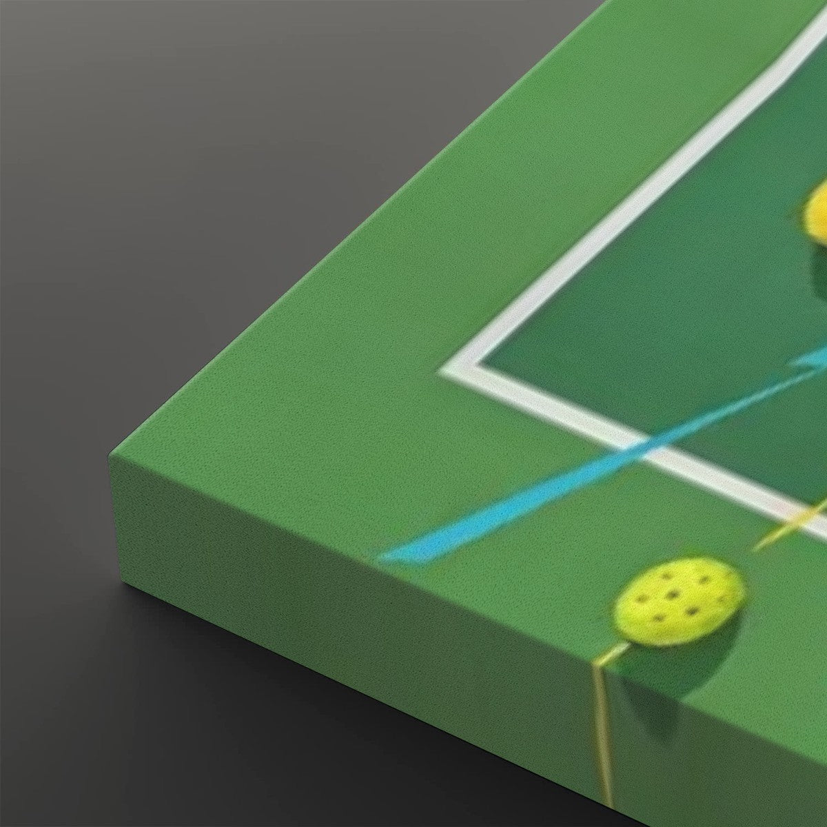 A close-up of a green canvas print showing a stylized  pickleball  design with white boundary lines, blue and yellow strokes, and tennis balls, photographed against a dark gray background.