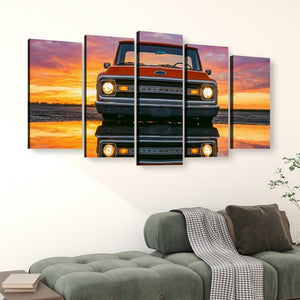 A five-panel canvas wall art set depicting a front view of an orange Chevrolet truck reflected on water at sunset, displayed above a green sofa in a living room setting.