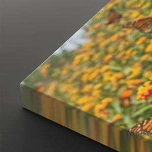 A close-up of a rectangular canvas or print showing a blurred outdoor floral scene with yellow flowers, green foliage, and butterfly wings, photographed on a dark gray background.