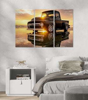 A three-panel canvas wall art print depicting a black  1956 Ford  F-100 vintage pickup truck on a reflective beach at sunset, displayed above a bed in a modern bedroom setting.