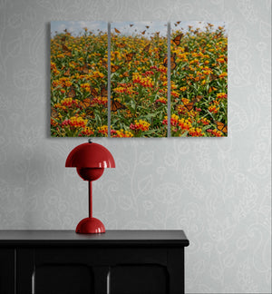 Triptych wall art of a floral scene with butterflies above a red lamp on a black surface.