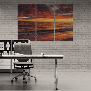 Modern office setup with a large triptych painting of a sunset over water on a brick wall.