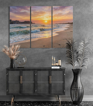 Triptych wall art of a beach sunset above a black cabinet with decorative items.