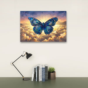 A rectangular wall art print showing a large blue butterfly over glowing clouds, displayed above a desk with a black lamp, books, and a small succulent against a light wall.
