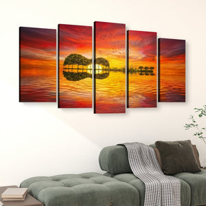 A 5-panel canvas wall art set depicting a vibrant sunset over water with tree reflections, displayed above a green sofa in a modern living room setting.