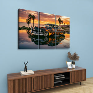 A three-panel canvas wall art print depicting a classic car with orange flames on its body, parked in front of palm trees at sunset, displayed above a wooden console table in a modern room setting.