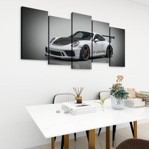 A 5-panel canvas wall art set depicting a black and white Porsche 911 GT3, displayed in a modern living room setting above a white dining table.