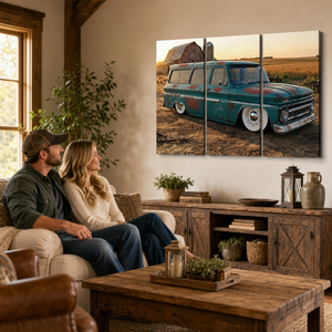 A three-panel canvas wall art print depicting a vintage teal 1966 Chevy Suburban Carryall in a rural field at sunset, displayed on a beige wall in a rustic living room setting with a couple sitting on a couch below.