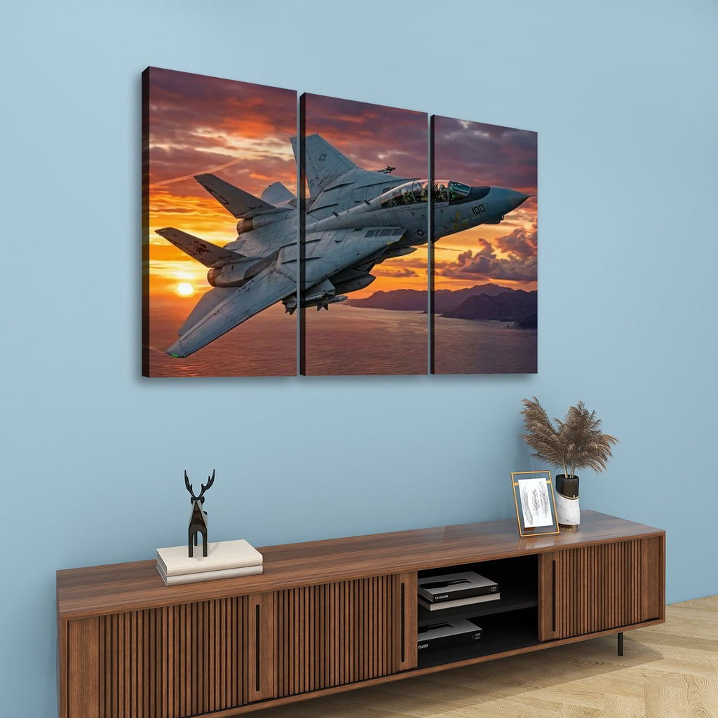 A three-panel canvas wall art set depicting a gray Grumman F-14 fighter jet flying over a sunset over water, displayed on a light blue wall above a wooden console table with decorative items.