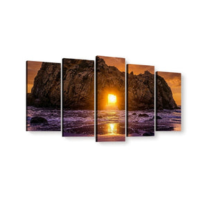 A five-panel canvas wall art set depicting a dramatic rocky coastline at sunset, with the sun low over the ocean and purple-toned waves in the foreground, shown against a plain white background.