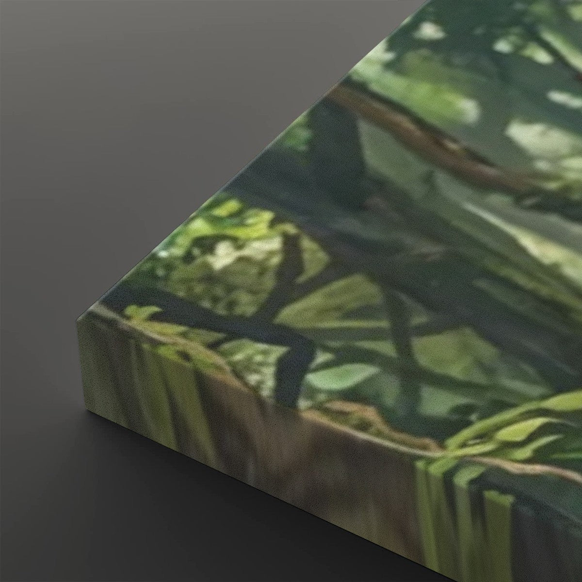 A close-up of a rectangular canvas or print showing a forest scene with green foliage and dark branches, photographed against a dark gray background.
