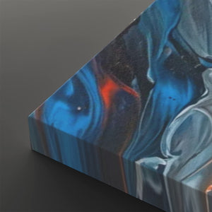 A close-up of a square canvas print showing an abstract fluid art design with swirling patterns of blue, black, white, and a small orange accent, photographed on a dark gray background.