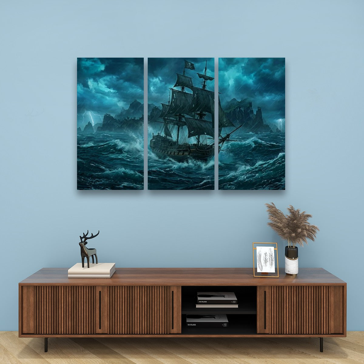 A three-panel canvas wall art set depicting a dark sailing ship battling stormy blue waves, displayed on a light blue wall above a wooden console table with decorative items.