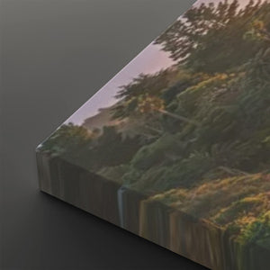 A rectangular canvas print shown at an angle on a dark gray background, featuring a scenic landscape with dense green trees and shrubs under warm golden light.