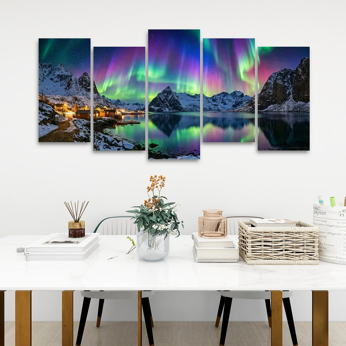 A five-panel canvas wall art set depicting a snowy mountain fjord at night with vivid green and purple aurora borealis over the water, displayed above a white dining table in a modern room setting.
