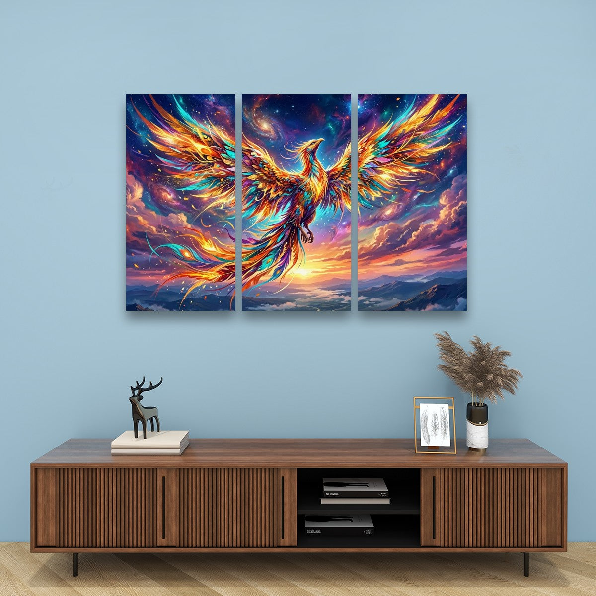 A three-panel canvas wall art set depicting a vibrant, colorful phoenix rising from a cosmic sky, displayed on a light blue wall above a wooden console table.