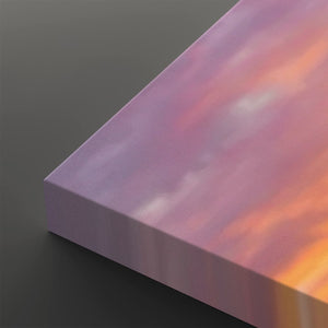 A close-up of a rectangular canvas or panel with a printed sunset sky design, showing pink, purple, orange, and yellow tones, photographed on a dark gray background.