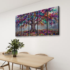 A four-panel canvas wall art set depicting a colorful, textured tree with a brown trunk and vibrant multicolored foliage, displayed on a white wall above a light wood dining table with chairs and a green plant.