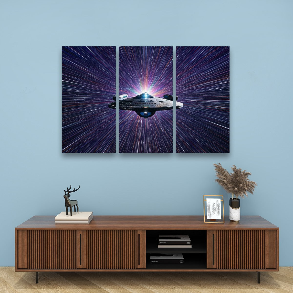 A three-panel canvas wall art set depicting a spaceship in a purple and blue starburst galaxy, displayed on a light blue wall above a wooden console table with decorative items.
