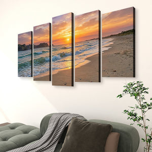 A five-panel canvas wall art set depicting a beach sunset with ocean waves, displayed above a green sofa in a living room setting.