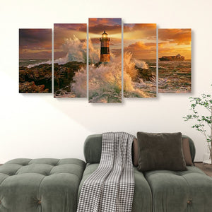 A five-panel canvas wall art set depicting a dramatic lighthouse scene with ocean waves, rocky shore, and a warm sunset sky, displayed above a green sofa in a living room setting.