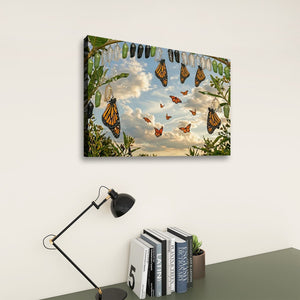 A rectangular wall art print showing monarch butterflies among green leaves against a blue sky with clouds, displayed above a desk with a black lamp and books in a styled interior setting.