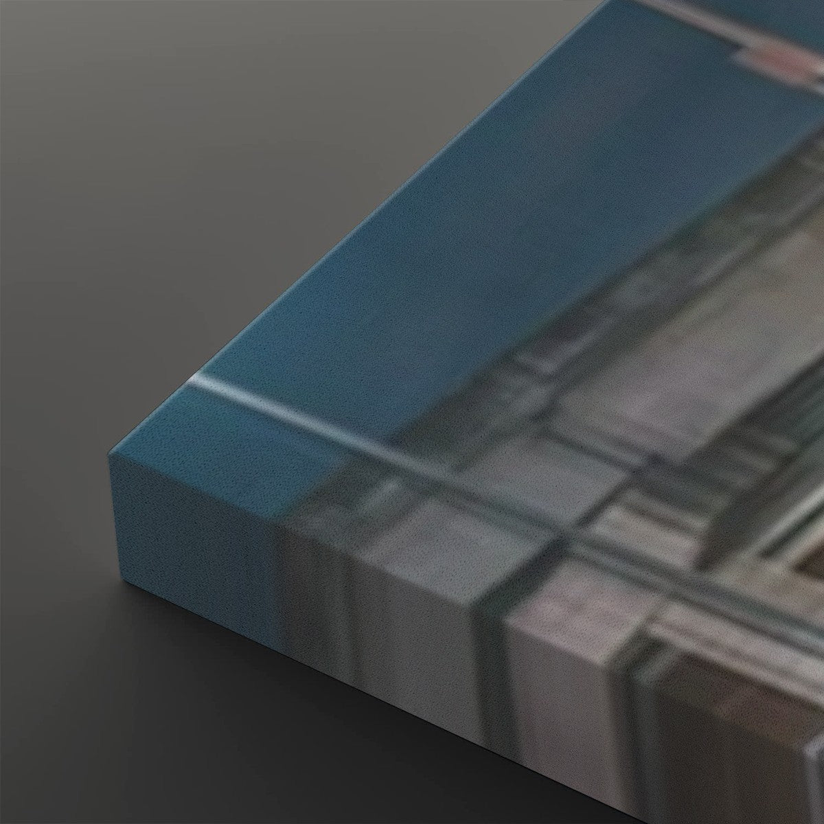 A close-up of a rectangular acrylic or glass art print block with a blue top surface and a blurred architectural or abstract scene printed on the side, resting on a dark gray surface.