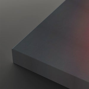 A close-up of a matte gray rectangular panel or block showing its corner and a subtle warm pinkish reflection on one side, set against a matching gray background.