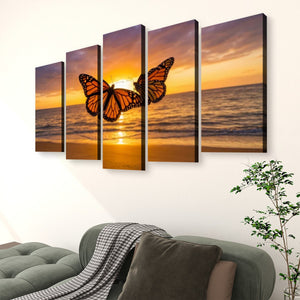A 5-panel canvas wall art set depicting two orange monarch butterflies flying over an ocean sunset, displayed on a white wall above a green sofa in a living room setting.