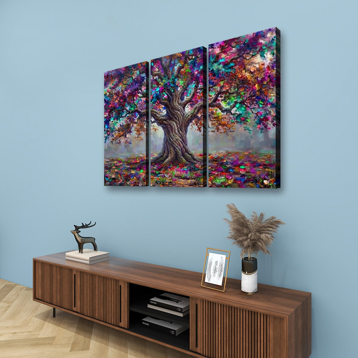 A three-panel canvas wall art set depicting a colorful, textured tree with vibrant autumn foliage, displayed on a light blue wall above a wooden console table.