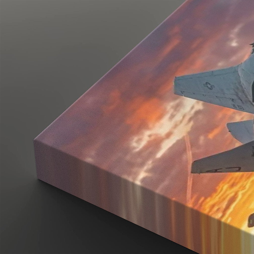 A close-up of a rectangular canvas print showing a sunset sky with orange and pink clouds and part of a fighter jet, photographed on a dark gray background.