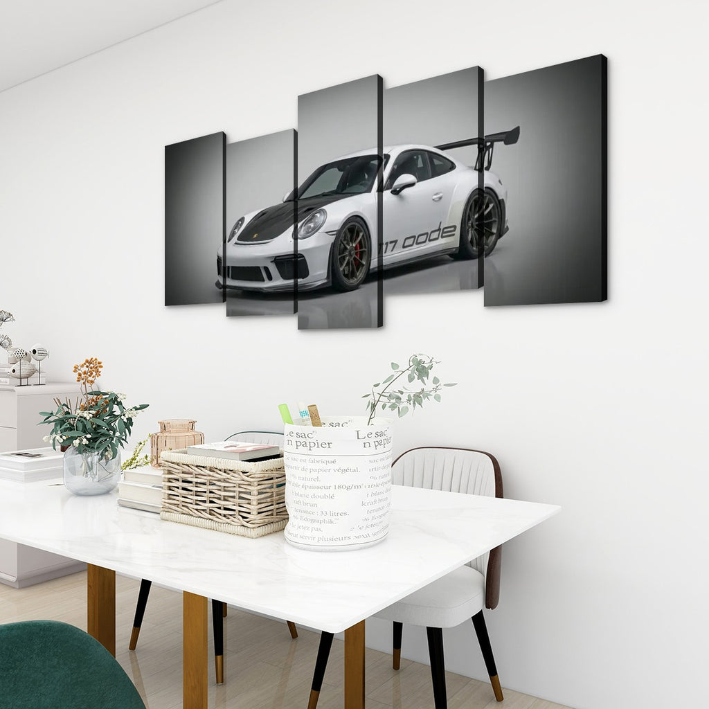 A 4-panel canvas wall art print depicting a white Porsche 911 with black accents, displayed in a modern dining room setting above a white table with chairs.