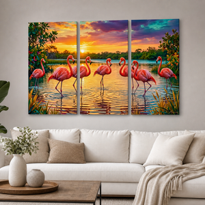 A three-panel canvas wall art set depicting a sunset flamingo scene, displayed on a light gray wall above a modern white sofa in a living room setting.