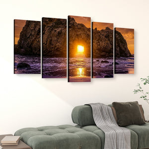 A five-panel canvas wall art set depicting a rocky coastline at sunset, displayed above a green sofa in a modern living room setting.
