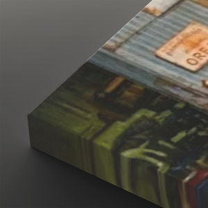 A close-up angled view of a rectangular canvas or print showing an abstract street-art style scene with muted green, blue-gray, black, and rusty orange tones, set against a dark gray background.